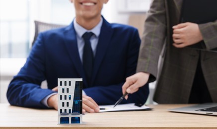Photo of Real estate agent working with client at desk in office, focus on house model