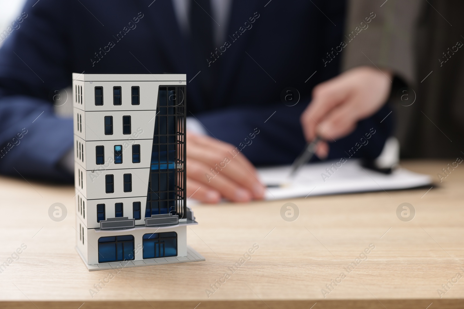 Photo of Real estate agent working with client at desk in office, focus on house model