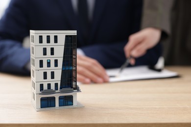 Photo of Real estate agent working with client at desk in office, focus on house model