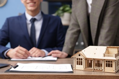 Photo of Real estate agent working with client at desk in office, focus on house model