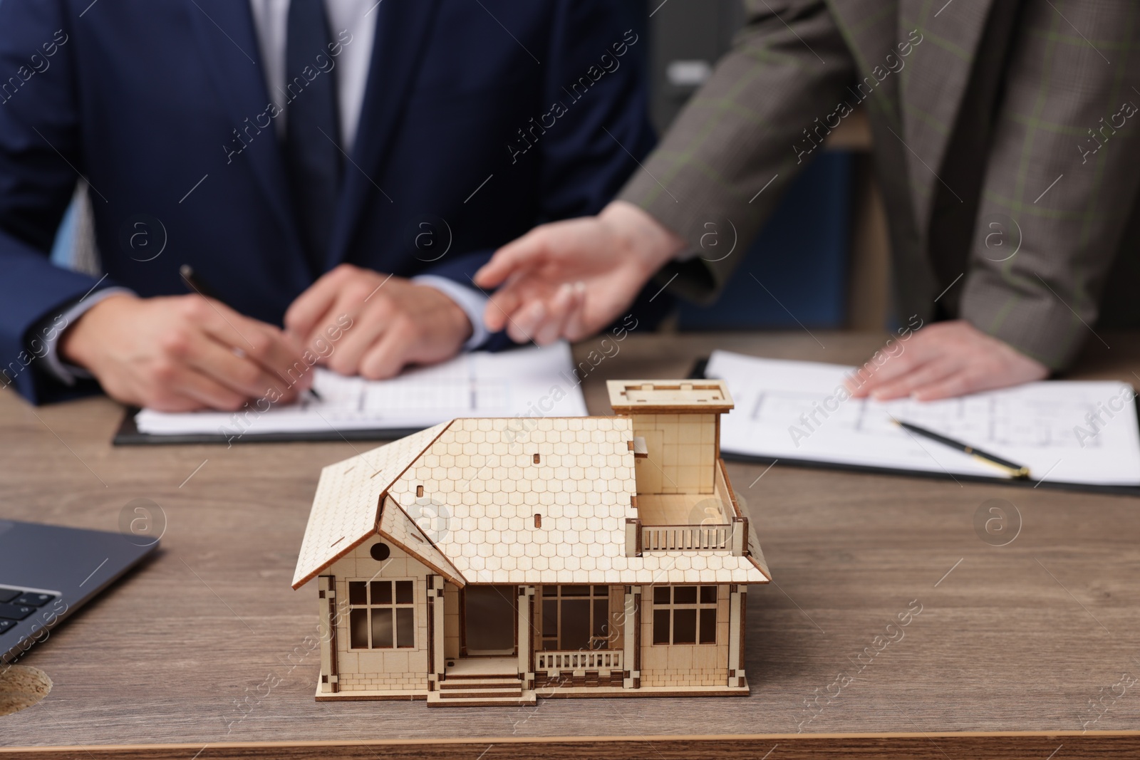 Photo of Real estate agent working with client at desk in office, focus on house model