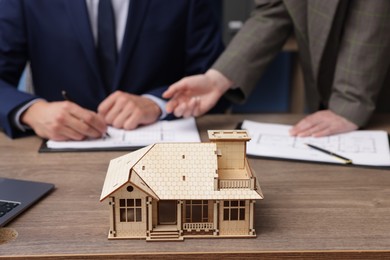 Photo of Real estate agent working with client at desk in office, focus on house model