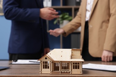 Photo of Real estate agent giving key to client at desk in office, focus on house model