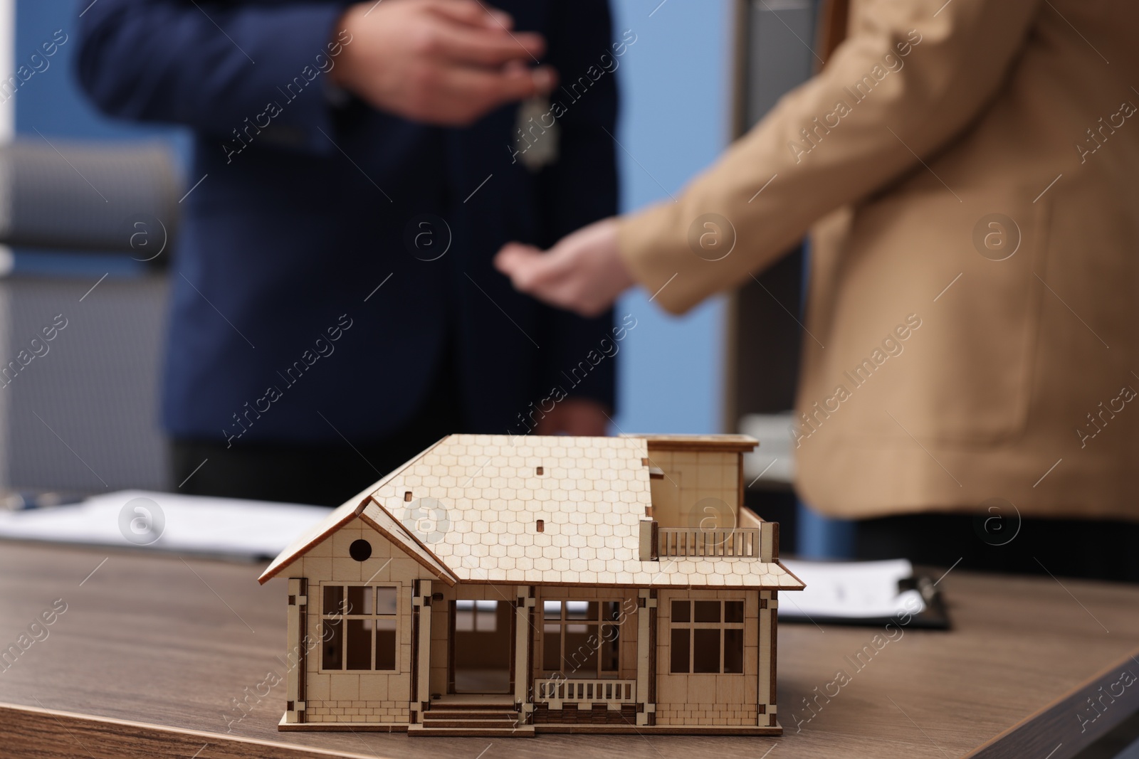 Real estate agent giving key to client at desk in office, focus on house model Photo of Real estate agent giving key to client at desk in office, focus on house model