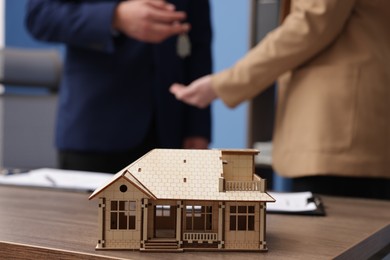 Photo of Real estate agent giving key to client at desk in office, focus on house model