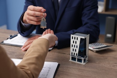 Photo of Real estate agent giving key to client at desk in office, focus on house model