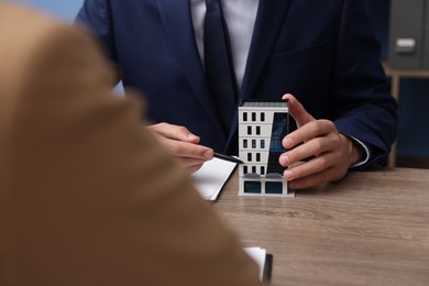 Photo of Real estate agent working with client at desk with house model in office, closeup