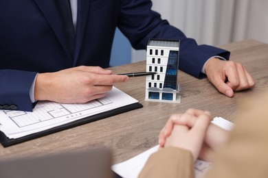 Photo of Real estate agent working with client at desk with house model in office, closeup