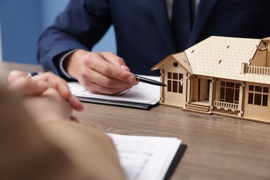 Photo of Real estate agent working with client at desk with house model in office, closeup