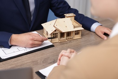 Photo of Real estate agent working with client at desk with house model in office, closeup