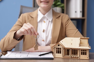 Photo of Real estate agent holding key and house model at desk in office, closeup
