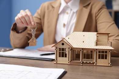 Photo of Real estate agent holding key at desk in office, focus on house model