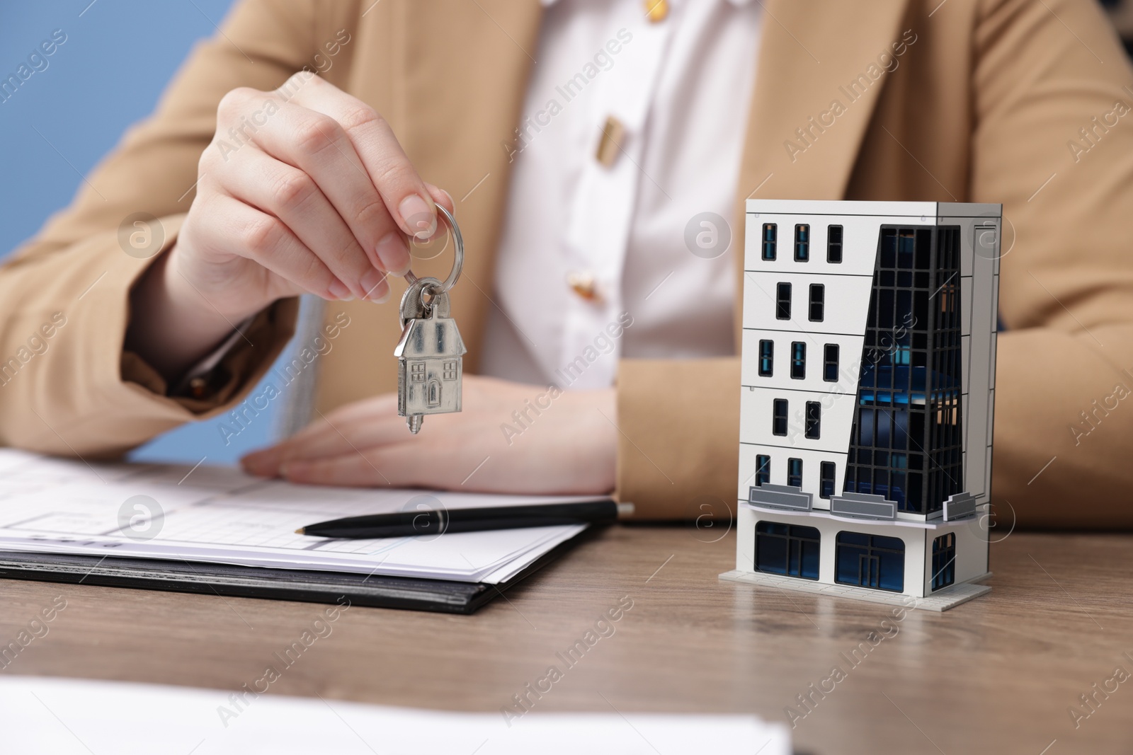 Photo of Real estate agent holding key and house model at desk in office, closeup