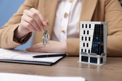 Photo of Real estate agent holding key and house model at desk in office, closeup