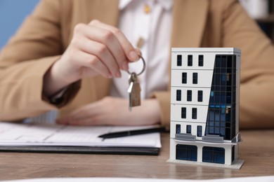Photo of Real estate agent holding key at desk in office, focus on house model