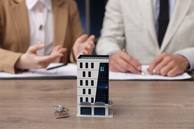 Photo of Real estate agent working with client at desk in office, focus on house model