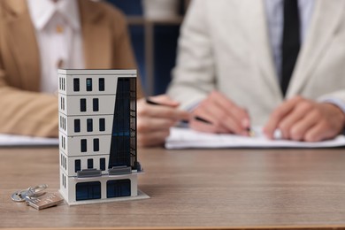 Photo of Real estate agent working with client at desk in office, focus on house model