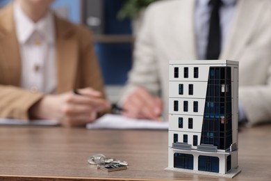 Photo of Real estate agent working with client at desk in office, focus on house model