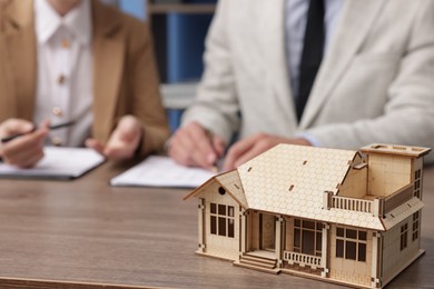 Photo of Real estate agent working with client at desk in office, focus on house model
