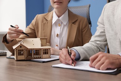 Photo of Real estate agent working with client at desk with house model in office, closeup