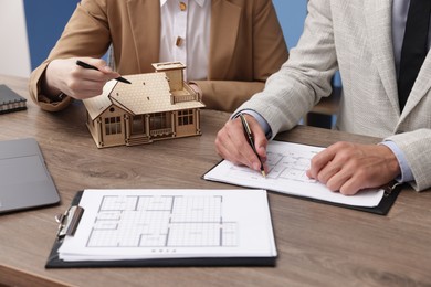 Photo of Real estate agent working with client at desk with house model in office, closeup
