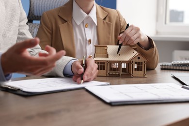 Photo of Real estate agent working with client at desk with house model in office, closeup