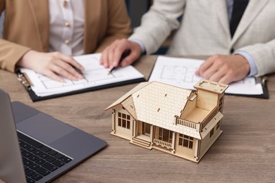 Photo of Real estate agent working with client at desk with house model in office, closeup