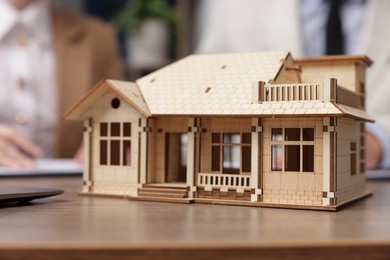 Photo of Real estate agent working with client at desk in office, focus on house model