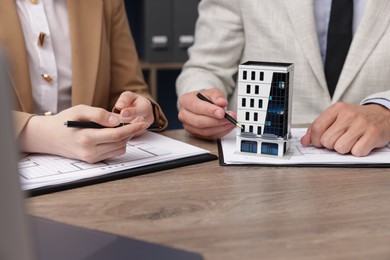 Photo of Real estate agent working with client at desk with house model in office, closeup