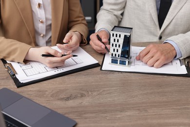 Photo of Real estate agent working with client at desk with house model in office, closeup