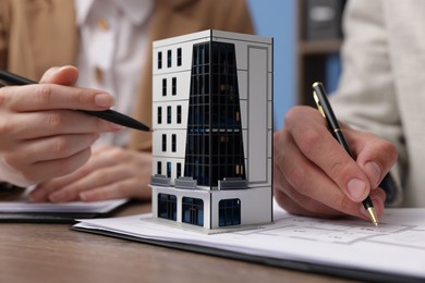 Photo of Real estate agent working with client at desk with house model in office, closeup