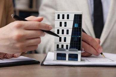 Photo of Real estate agent working with client at desk with house model in office, closeup