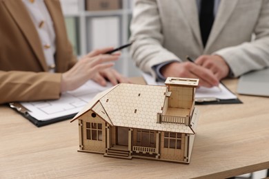 Photo of Real estate agent working with client at desk in office, focus on house model