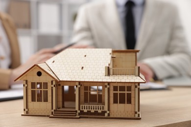Photo of Real estate agent working with client at desk in office, focus on house model