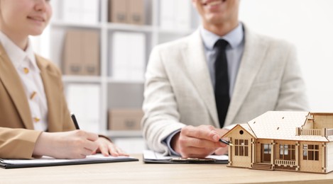 Photo of Real estate agent working with client at desk in office, focus on house model