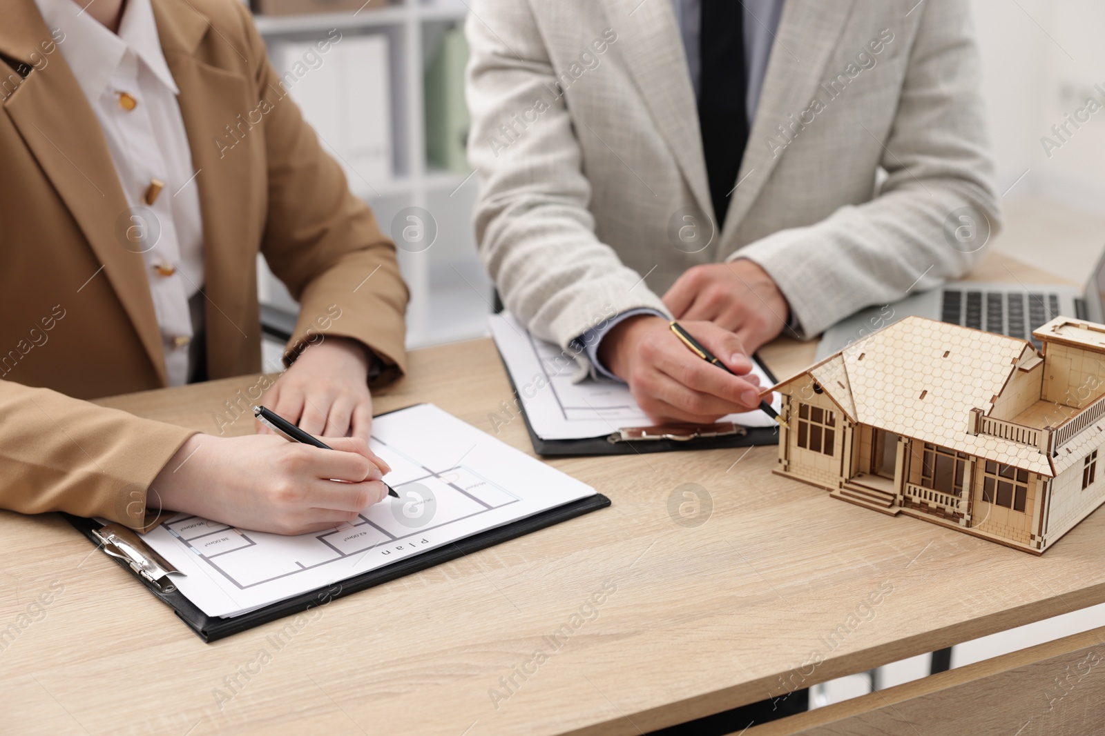 Real estate agent working with client at desk with house model in office, closeup Photo of Real estate agent working with client at desk with house model in office, closeup