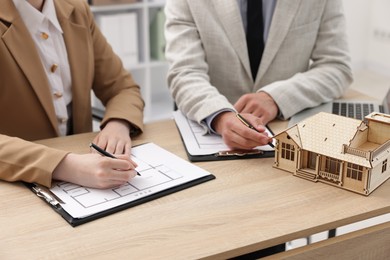 Photo of Real estate agent working with client at desk with house model in office, closeup