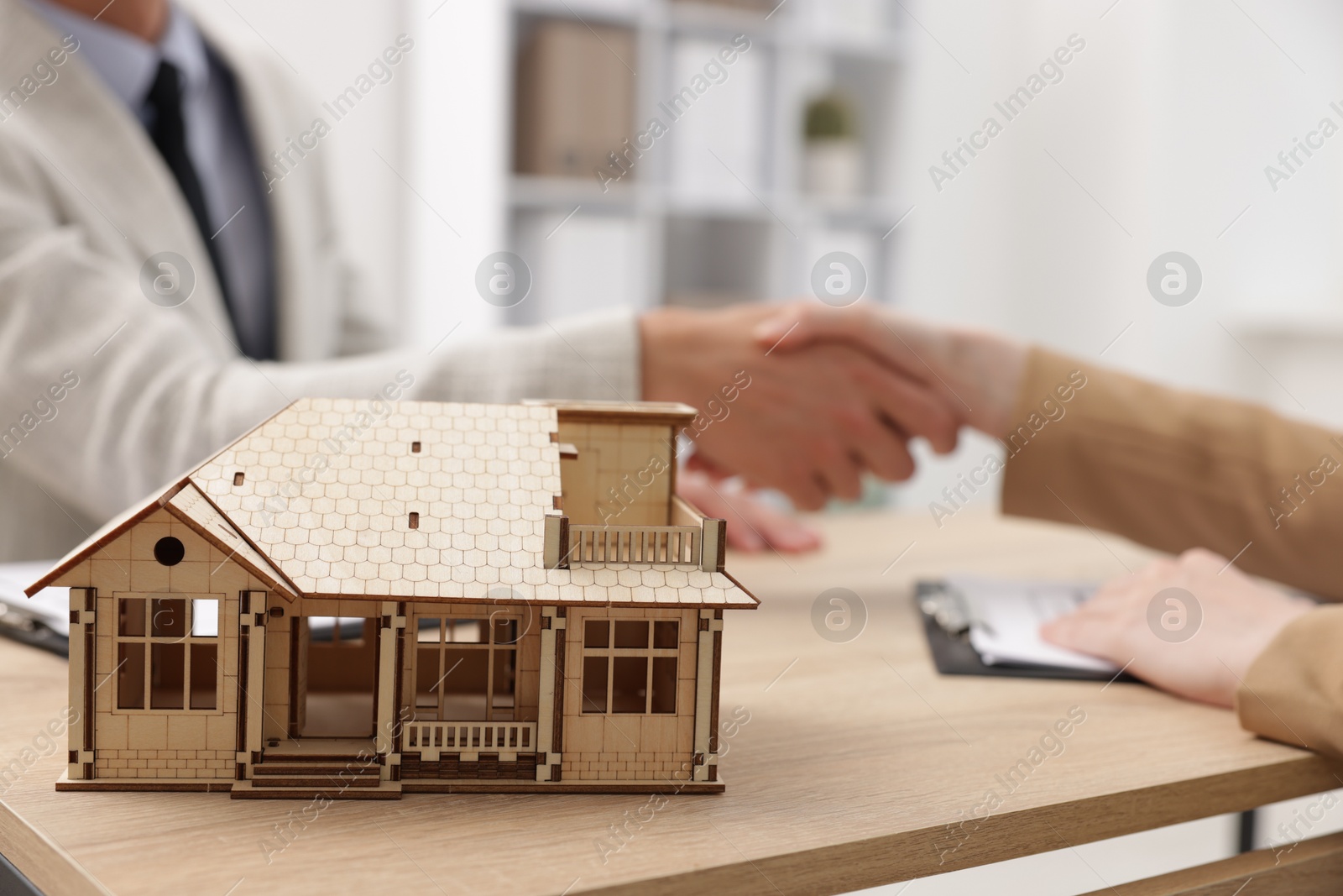Real estate agent and client shaking hands at desk in office, focus on house model Photo of Real estate agent and client shaking hands at desk in office, focus on house model