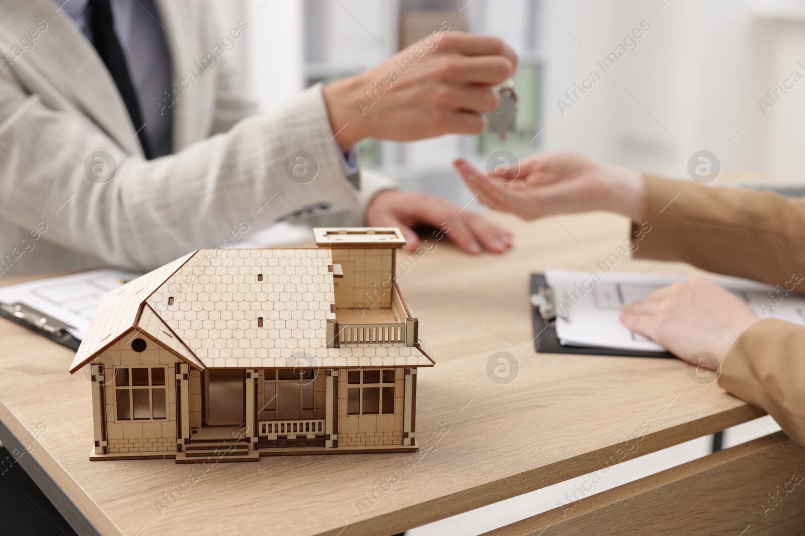 Real estate agent giving key to client at desk in office, focus on house model Photo of Real estate agent giving key to client at desk in office, focus on house model