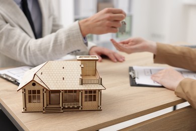 Photo of Real estate agent giving key to client at desk in office, focus on house model