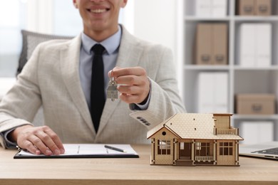Photo of Real estate agent holding key at desk in office, focus on house model