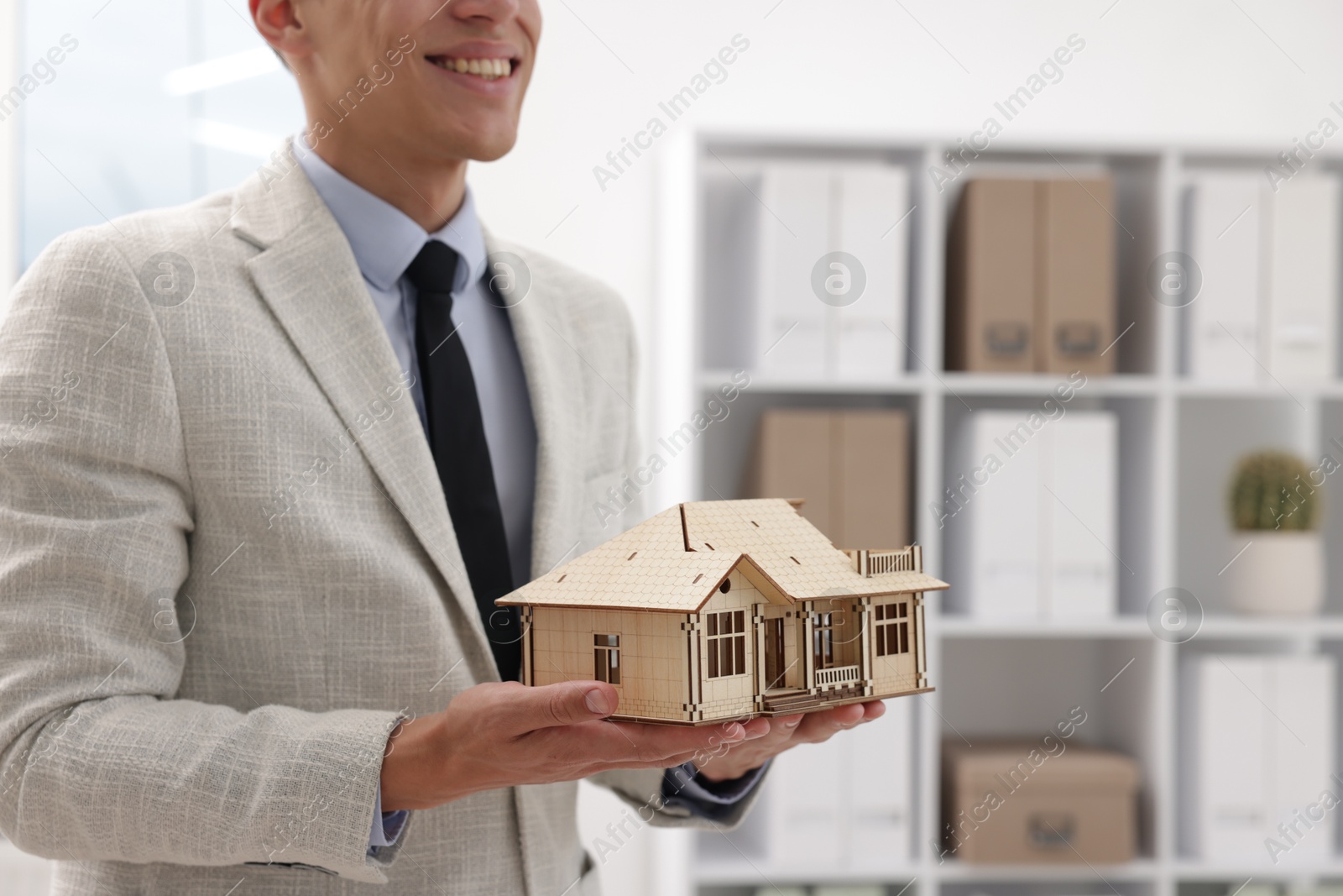 Real estate agent holding house model in office, closeup. Space for text Photo of Real estate agent holding house model in office, closeup. Space for text