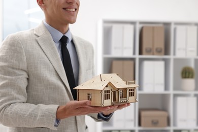 Photo of Real estate agent holding house model in office, closeup. Space for text