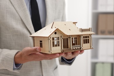 Photo of Real estate agent holding house model in office, closeup
