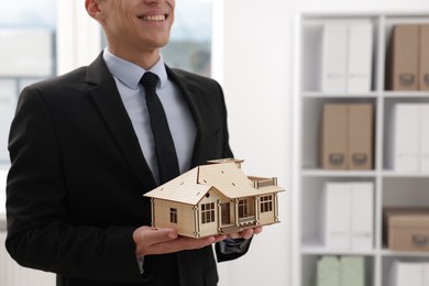 Photo of Real estate agent holding house model in office, closeup. Space for text