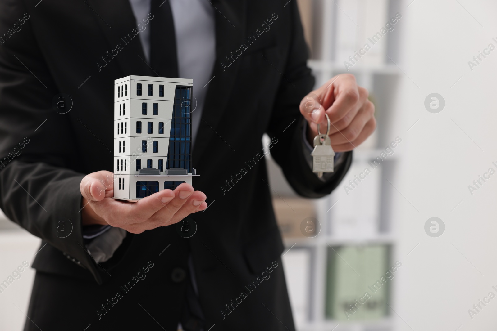 Real estate agent holding house model and key in office, closeup Photo of Real estate agent holding house model and key in office, closeup