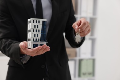 Photo of Real estate agent holding house model and key in office, closeup