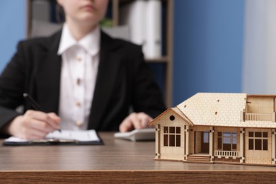 Photo of Real estate agent working at desk in office, focus on house model