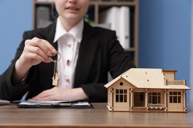 Photo of Real estate agent holding key and house model at desk in office, closeup