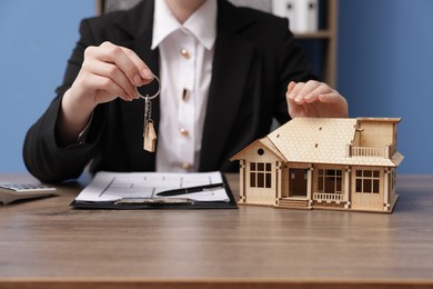 Photo of Real estate agent holding key and house model at desk in office, closeup